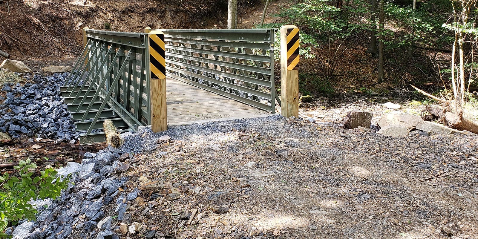 OSCO ReadySpan pedestrian bridge in a wooded area spanning a creek with rocks