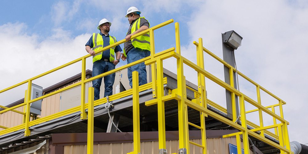 Two men in safety gear standing on OSCO ReadySeries platform featuring handrails, guardrails, stairs and ladders