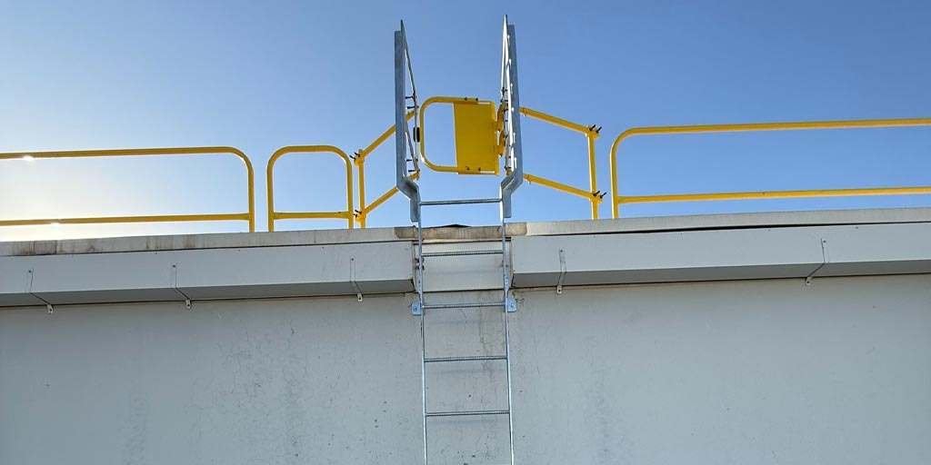 Fixed aluminum ladder and safety gate on the side of an exterior warehouse wall.