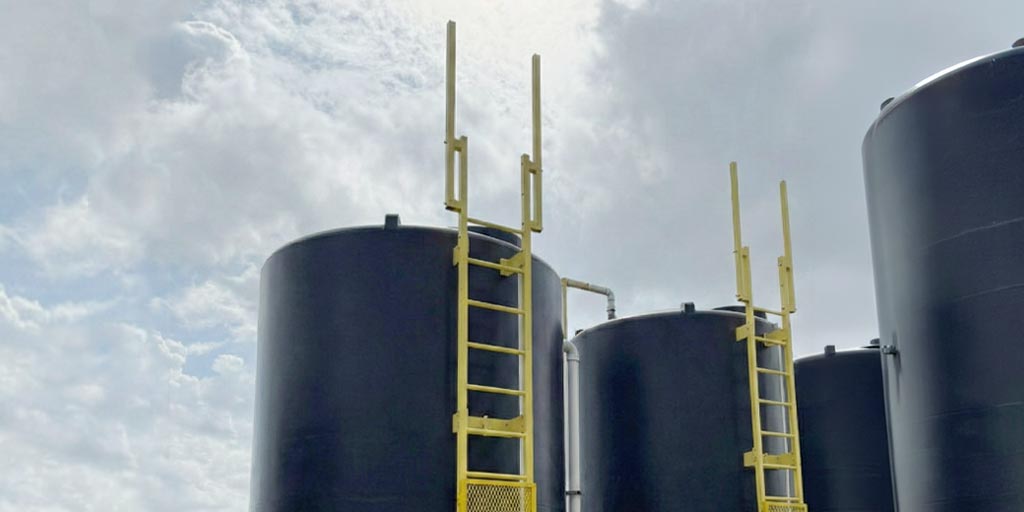 Fixed composite ladders on the side of black metal tanks with sky in background.
