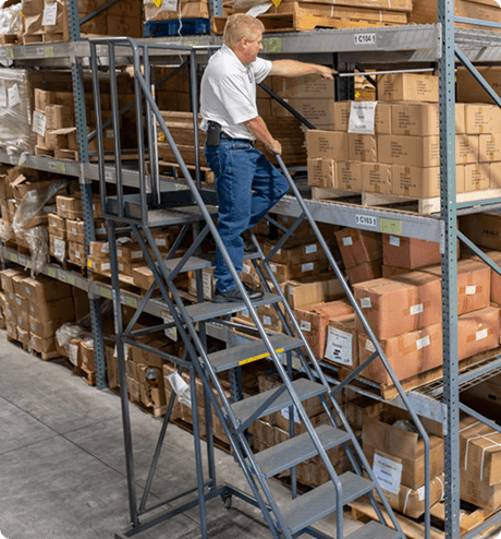 Man utilizing a rolling ladder to reach the third level of an industrial storage shelf